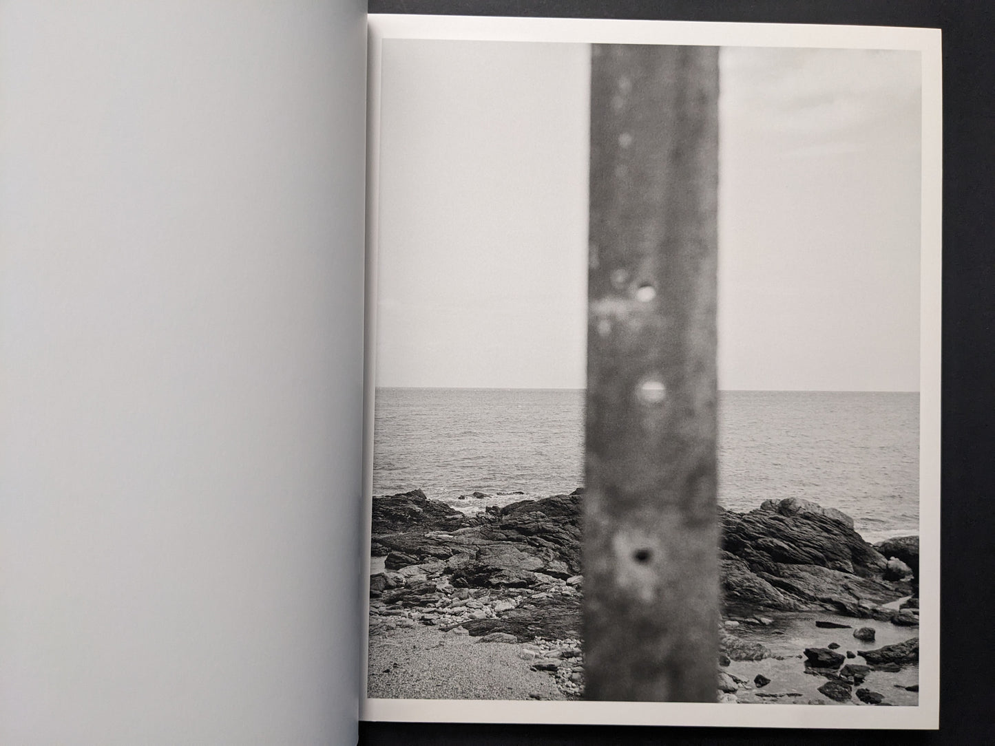 Interior photograph showing a rocky coastline and calm sea, partly obscured by a blurred vertical element.