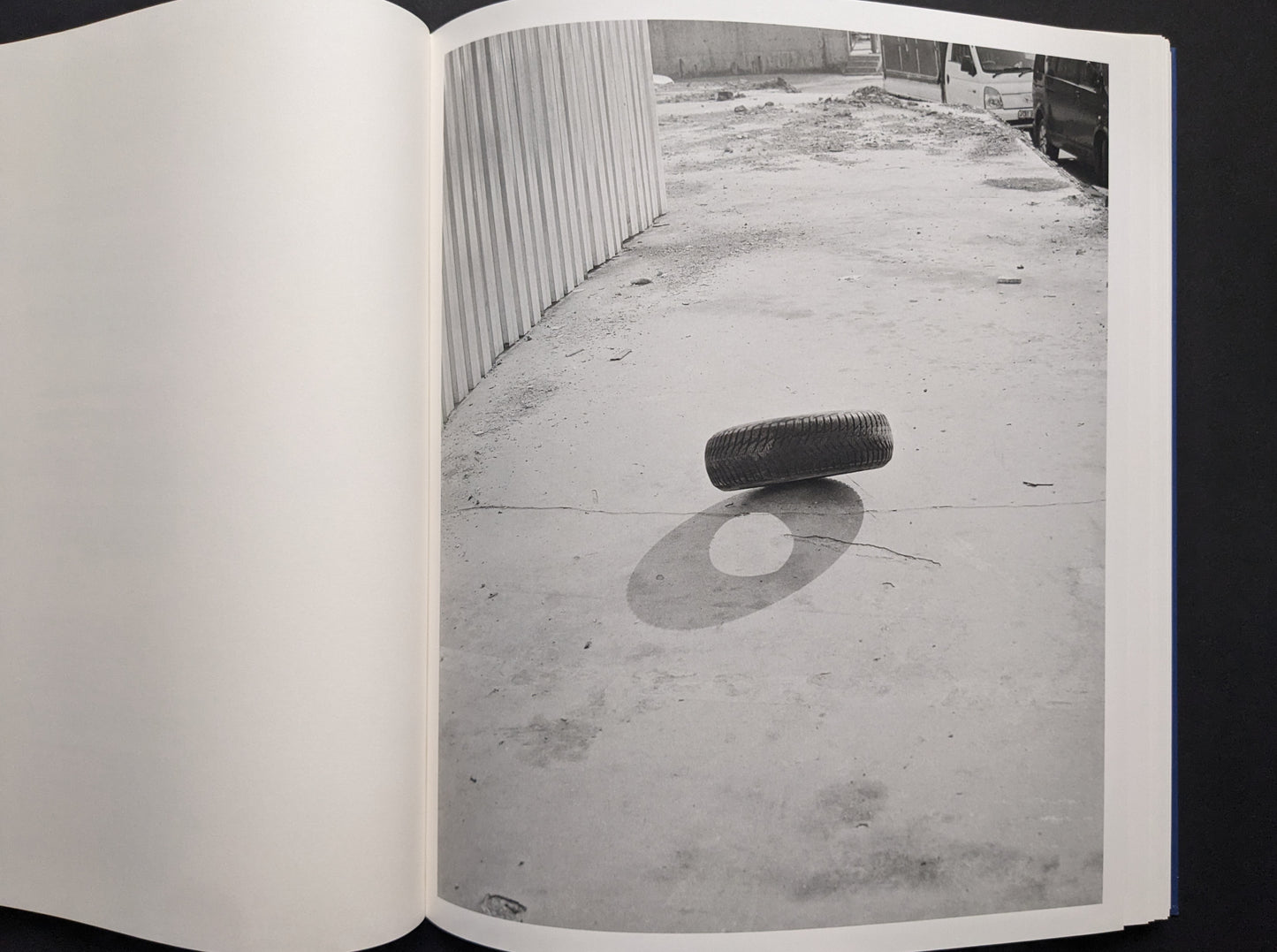 Black-and-white photograph of a tire balanced on its edge, casting a sharp shadow.
