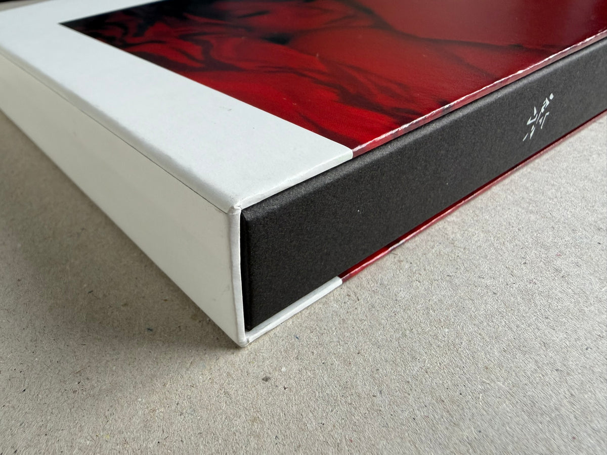 Close-up of the corner of the Surveillance – Tsutomu Yamagata book or box, showing a white outer sleeve, black side panel, and red printed cover edge.