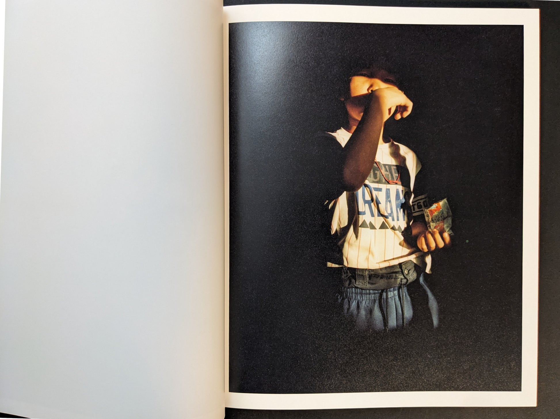 Photobook spread with a child portrait emerging from darkness, lit by a strong beam of light.