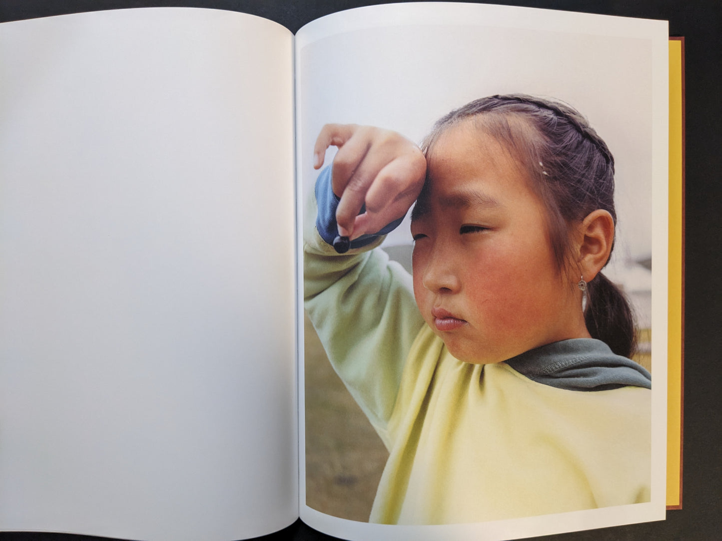 Portrait of a young girl holding a small dark object near her forehead against a pale sky.