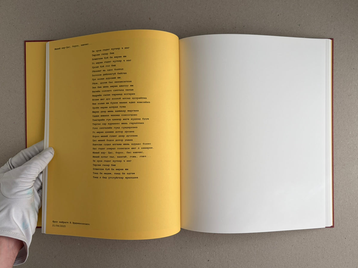 Open book spread from süü – Taemin Ha, showing a yellow left page with Mongolian text and a blank white right page, held open by a gloved hand.