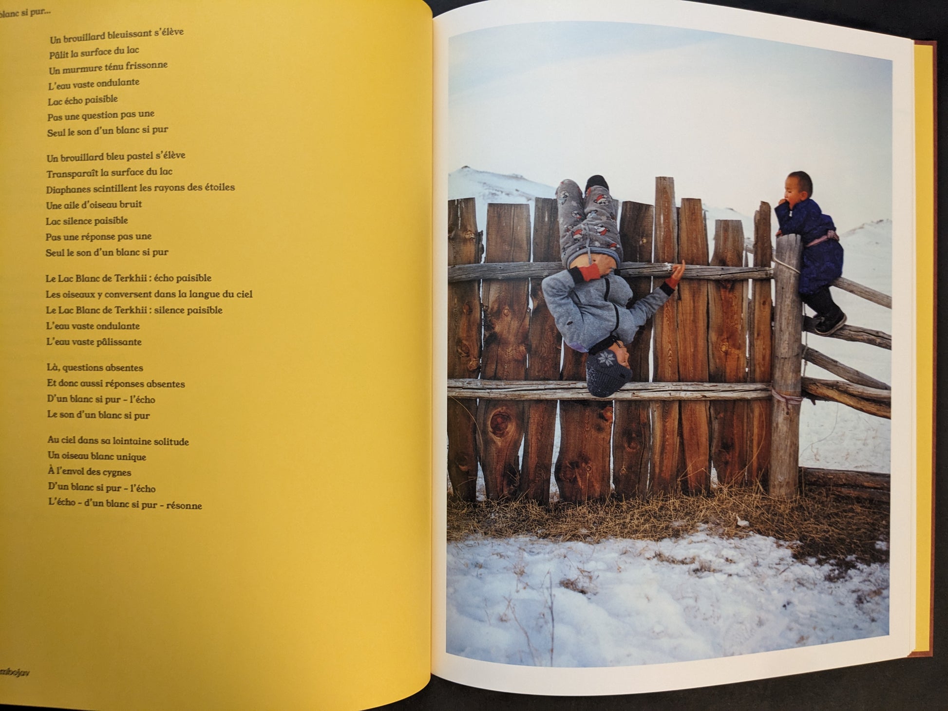 Photobook spread from süü by Taemin Ha with a poem page on yellow paper facing a winter photograph of two children on a wooden fence in a snowy landscape.
