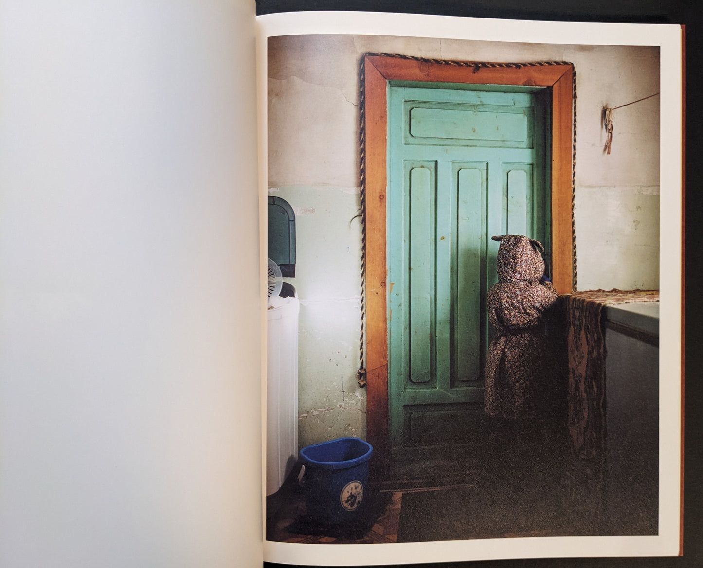 Domestic interior with a turquoise door and a small figure in a patterned coat facing the door.
