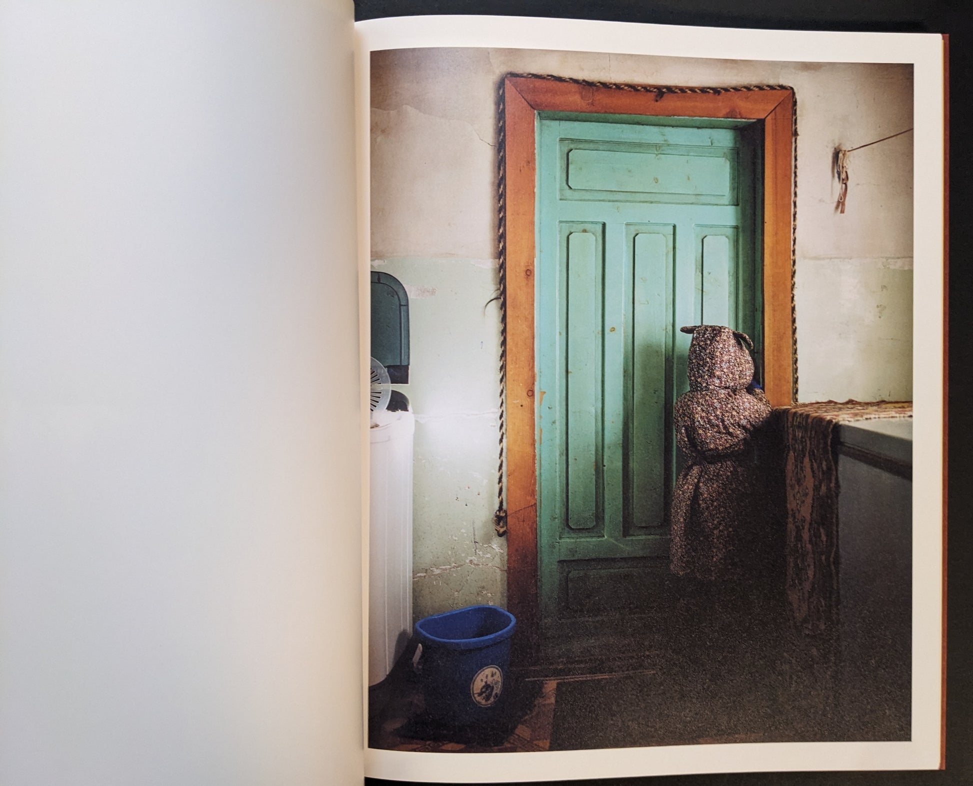 Domestic interior with a turquoise door and a small figure in a patterned coat facing the door.