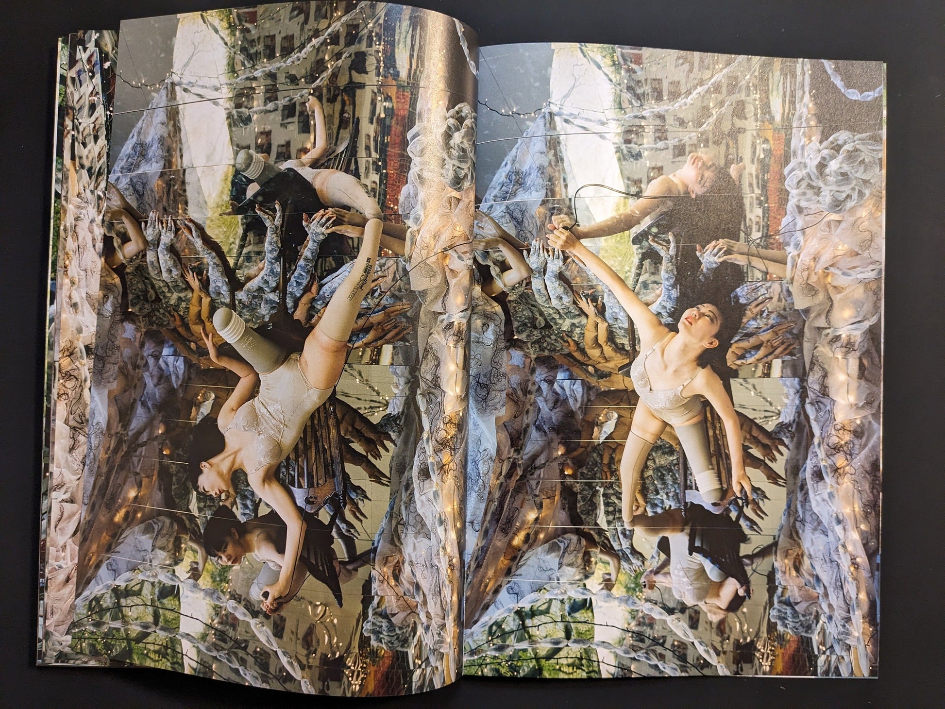 Double-page spread of suspended self-portraits with sculptural hand forms and reflective surfaces