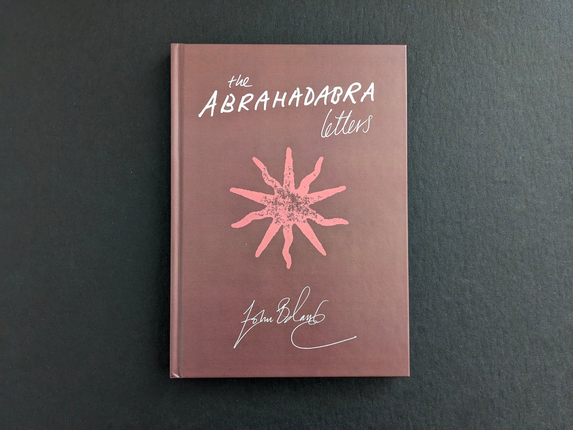 Front cover of The Abrahadabra Letters by John Balance and Anthony Blokdijk, with pink title lettering and signature-style design on a brown clothbound cover.