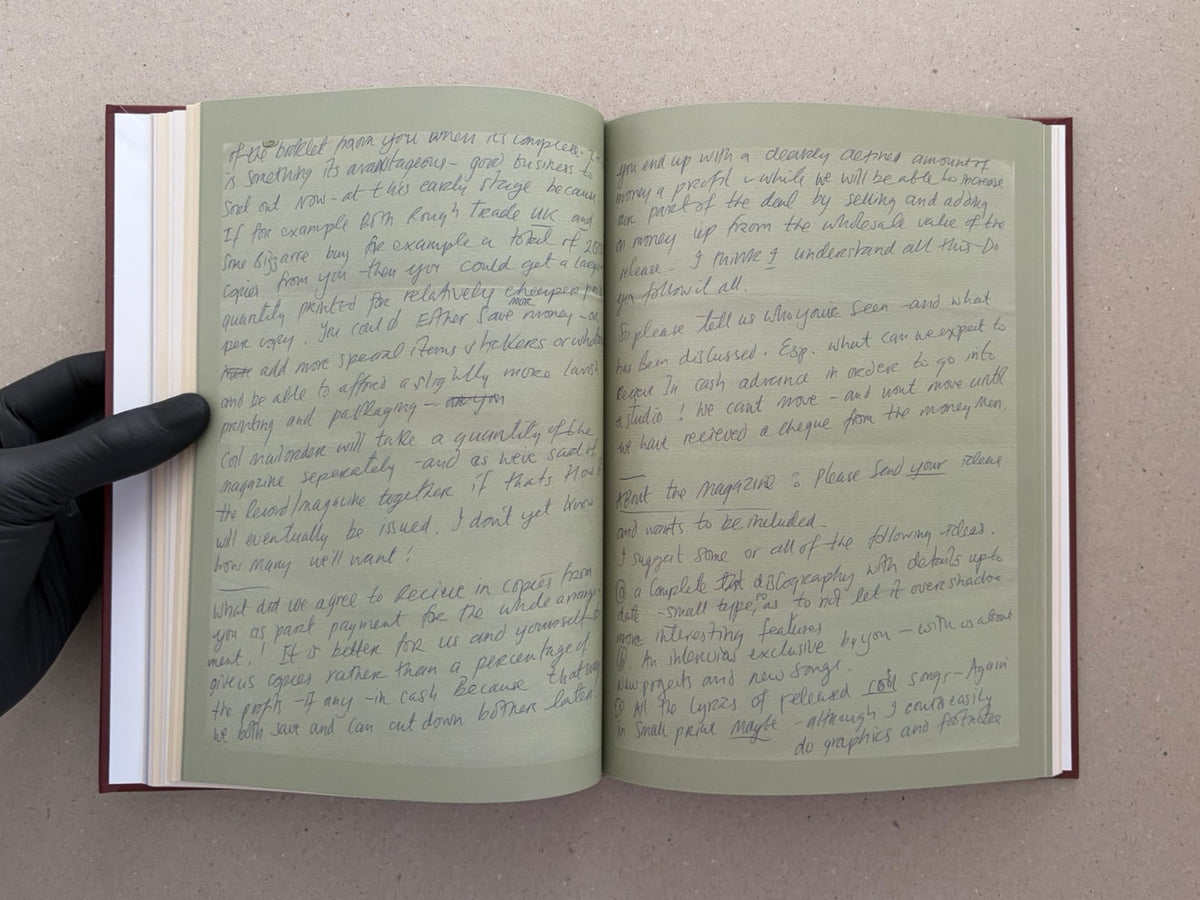 Open spread of The Abrahadabra Letters showing handwritten letter pages in a hardcover book, with a gloved hand holding the left side open.