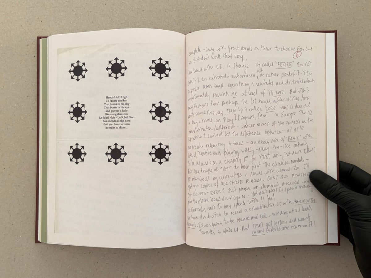 Open spread from The Abrahadabra Letters showing a printed page with repeated black symbols and a handwritten letter page, with a gloved hand holding the book open.