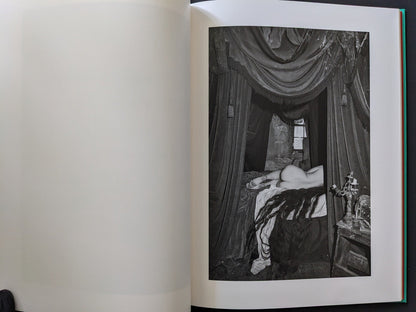 Figure seen nude from the back among heavy drapery and architectural arches.