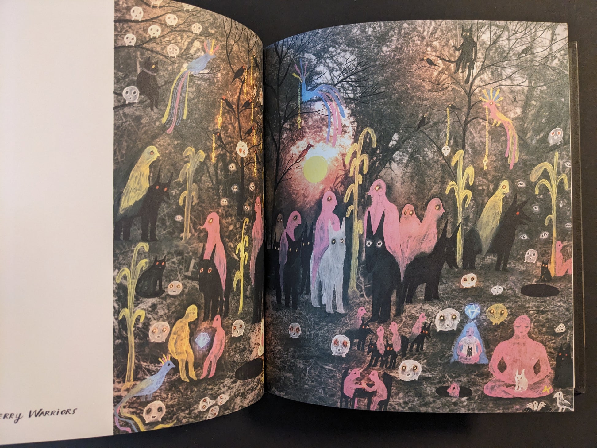 Full spread from The Fire That Drank The Shadow by Julia Soboleva showing a forest scene populated by colorful figures and animals, floating skull-like faces, and stylized birds around a bright central light.