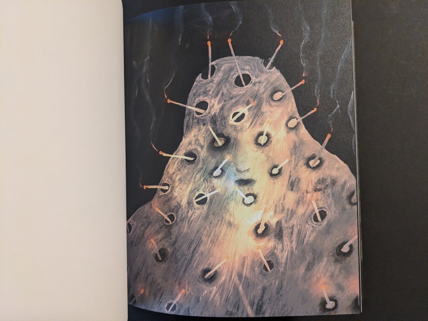 Artwork from The Fire That Drank The Shadow by Julia Soboleva showing a pale face-like form pierced with many smoking matchsticks against a dark background.