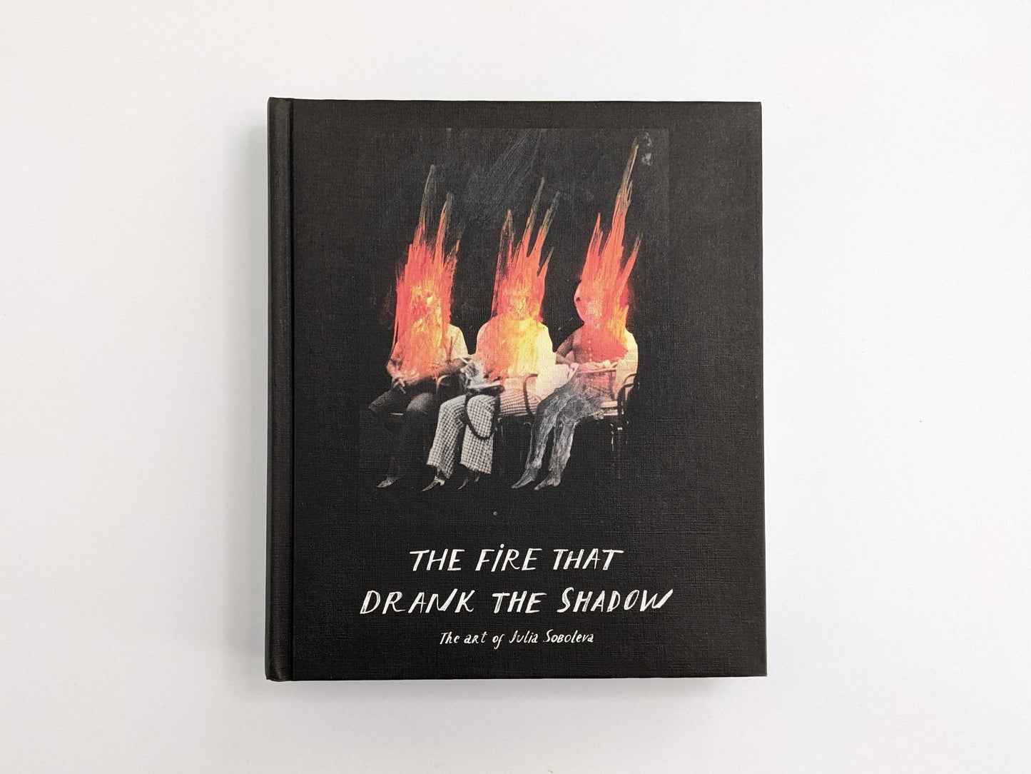 Cover of The Fire That Drank The Shadow: The Art of Julia Soboleva, showing three seated figures with flame-like heads on a white background.