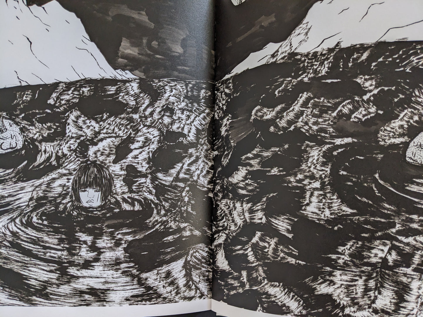 Two-page spread from “The Life of Namazuko” showing a young girl’s head floating in a dark, turbulent sea illustrated in black and white.