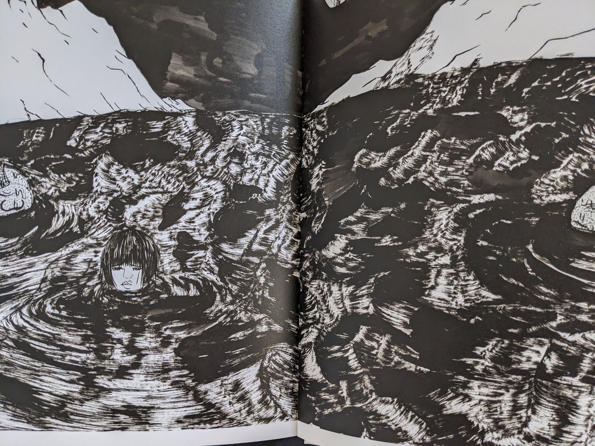 Two-page spread from “The Life of Namazuko” showing a young girl’s head floating in a dark, turbulent sea illustrated in black and white.