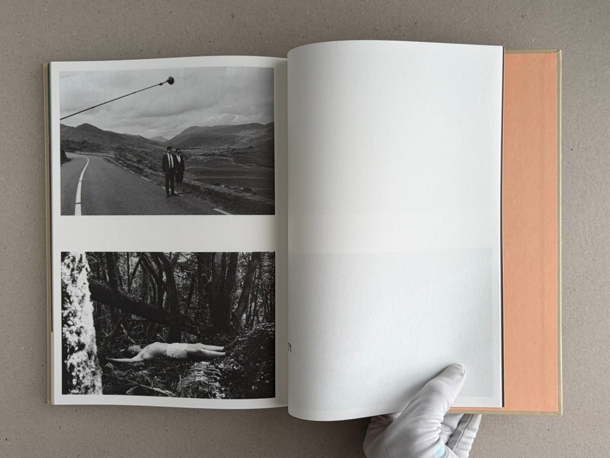 Open The Lobster Screenplay Book showing black-and-white film stills on the left page and a blank right page, with a gloved hand holding the book open.