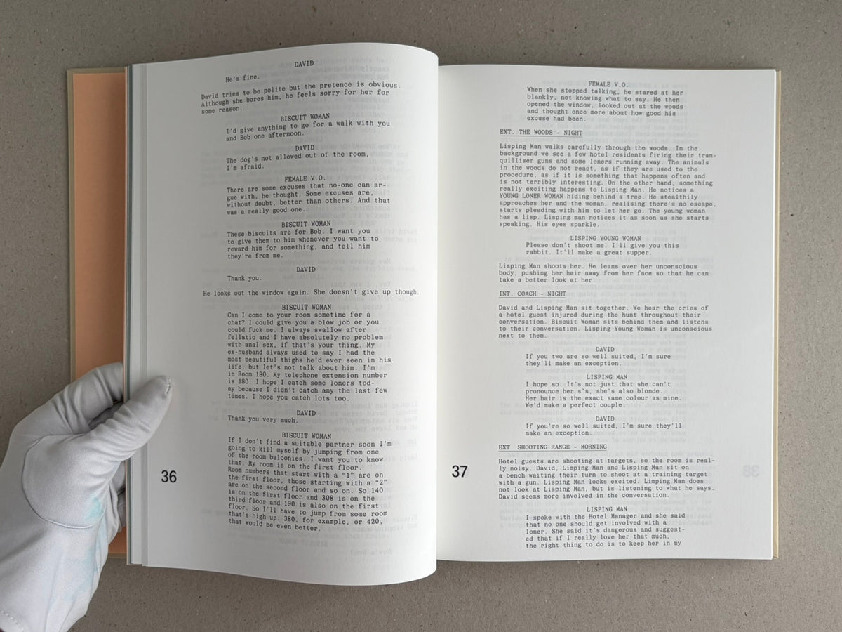 Open spread of The Lobster screenplay book, showing pages 36 and 37 with screenplay text and a gloved hand holding the lower left corner.