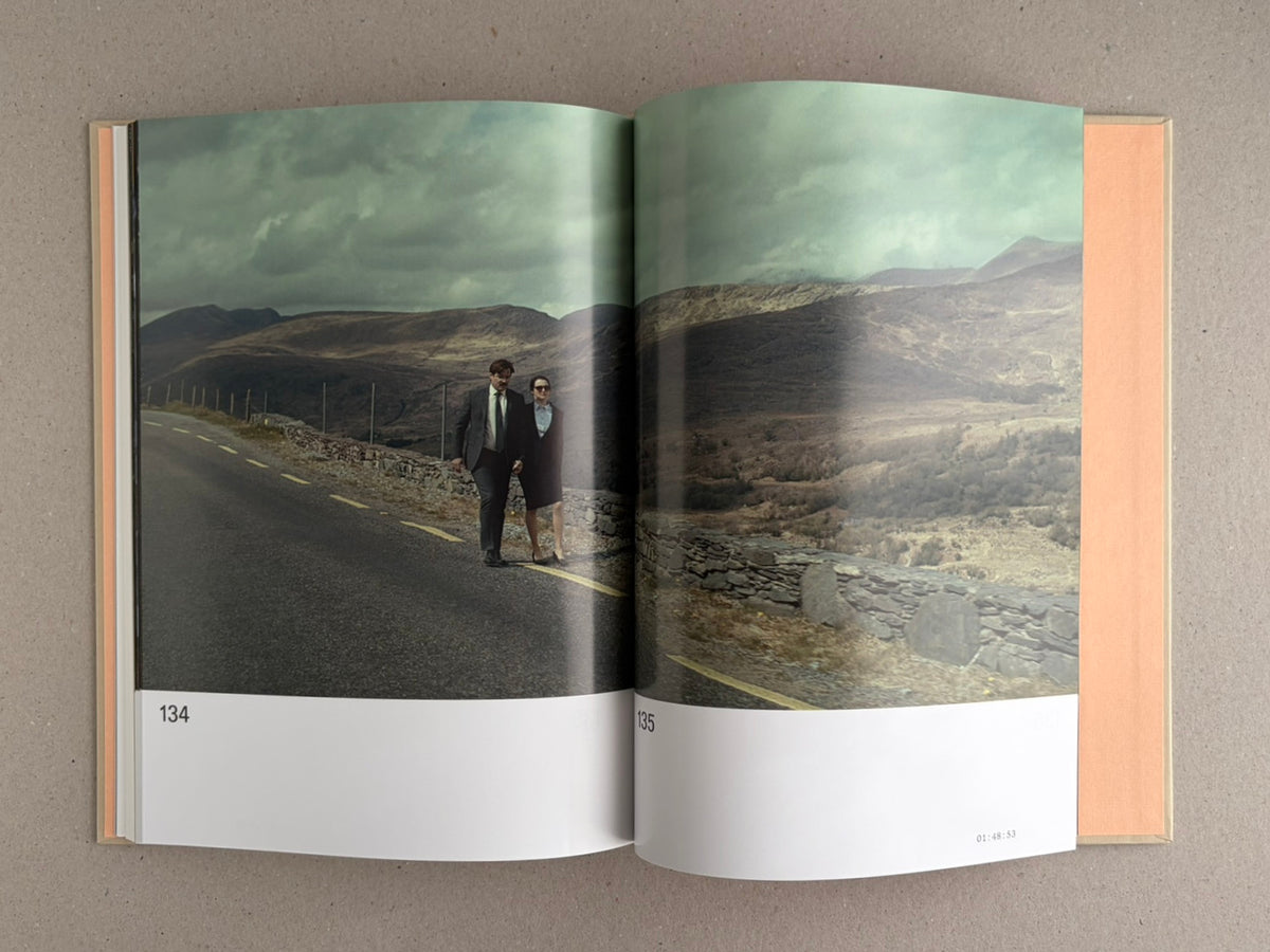 Open spread from The Lobster Screenplay Book showing a landscape photograph across pages 134-135, with two people standing on a road in a mountainous setting.