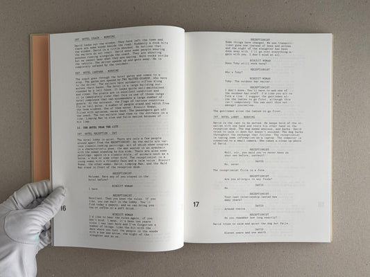 Open spread of The Lobster Screenplay Book showing screenplay text on pages 16 and 17, with a gloved hand holding the lower left corner.