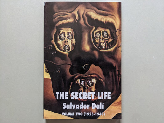 Front cover of "The Secret Life: Volume Two (1925–1940)" by Salvador Dalí, featuring a surreal painting of a distorted face filled with miniature skulls.