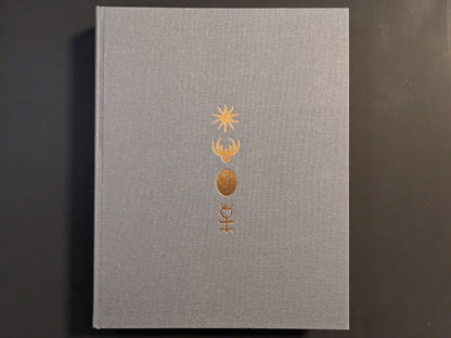 Front cover of The Universe is a Haunted House: COIL through their art & archives, gray cloth hardcover with gold embossed symbols.