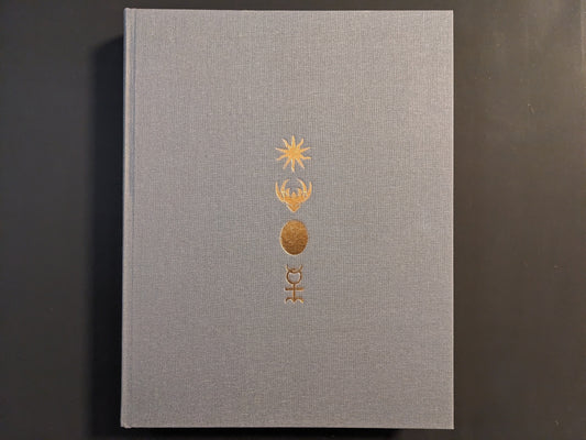 Front cover of The Universe is a Haunted House: COIL through their art & archives, gray cloth hardcover with gold embossed symbols.