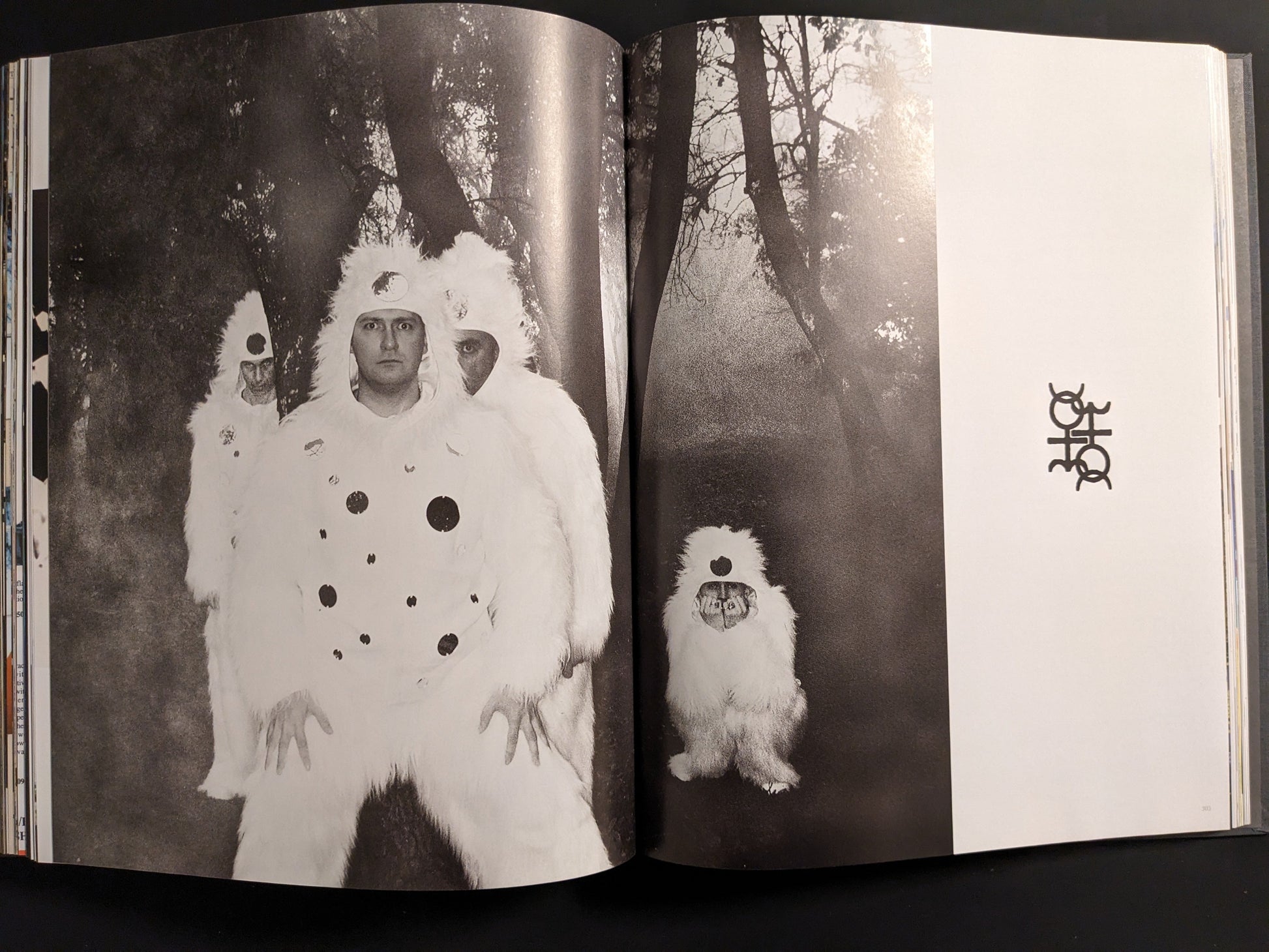 Black and white photo of two members of Coil in surreal white costumes with black dots, standing in a forest.