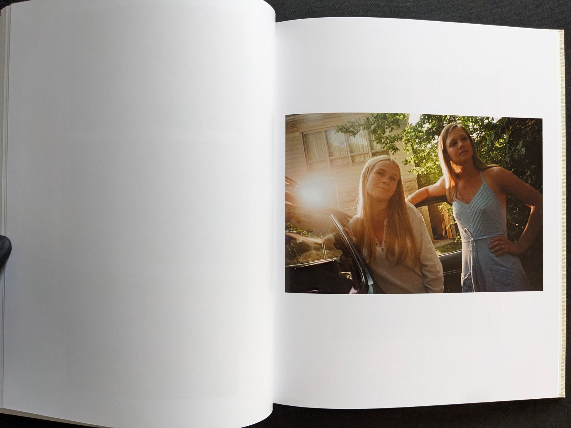 Interior page from The Virgin Suicides book showing two girls standing beside a car in warm afternoon light.