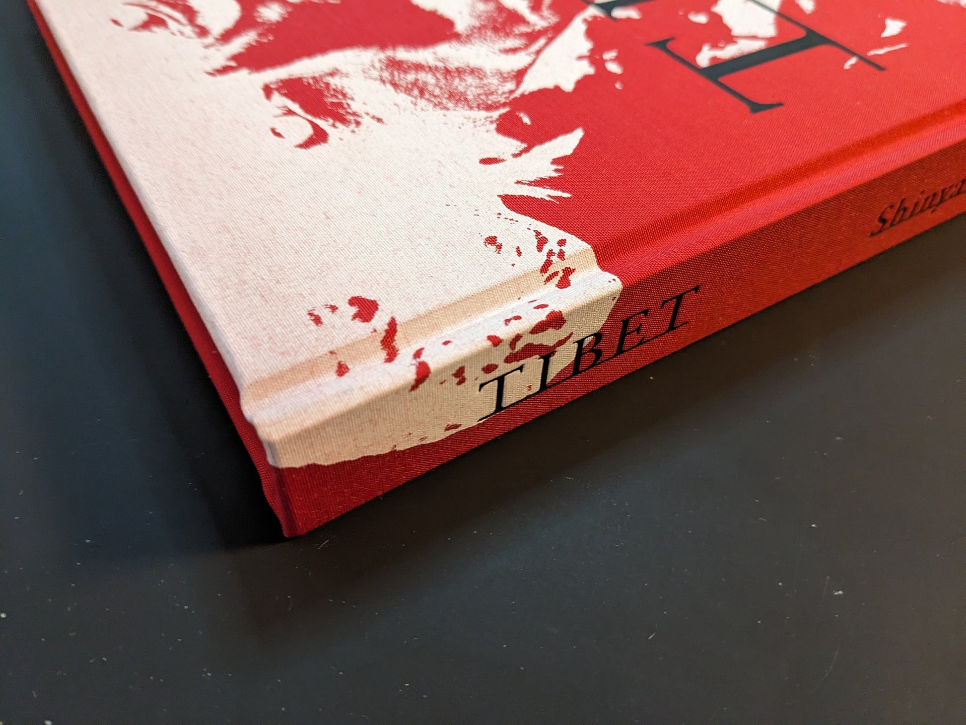 Close-up of the spine and lower corner of the photobook “TIBET” by Shinya Arimoto, highlighting the red-and-cream cloth cover and printed title.
