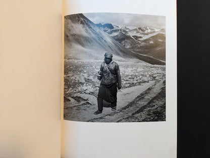 Inside page from “TIBET” depicting a solitary person walking along a rough mountain path in a high-altitude landscape.