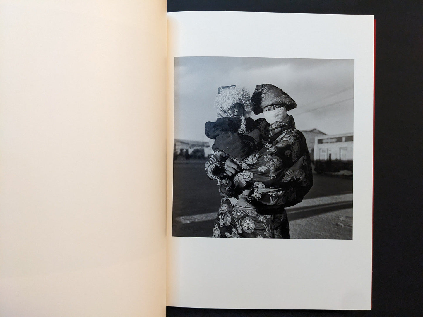 Inside page from “TIBET” depicting a woman in a richly patterned coat carrying a small child in her arms on a street.