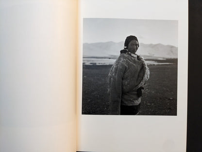 Inside page from “TIBET” featuring a woman in a heavy coat standing alone on a high plateau with distant mountains behind her.