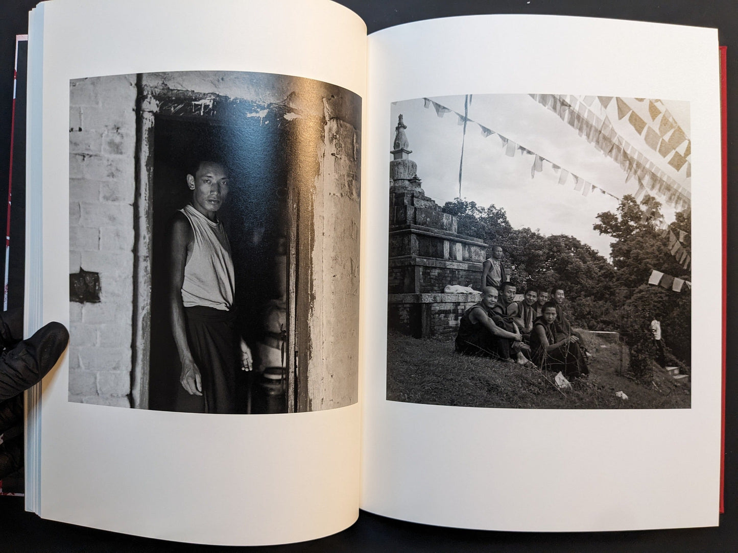 Spread from “TIBET” showing a monk standing in a doorway in one image and a group of young monks sitting on the grass near a stupa and prayer flags in the other.