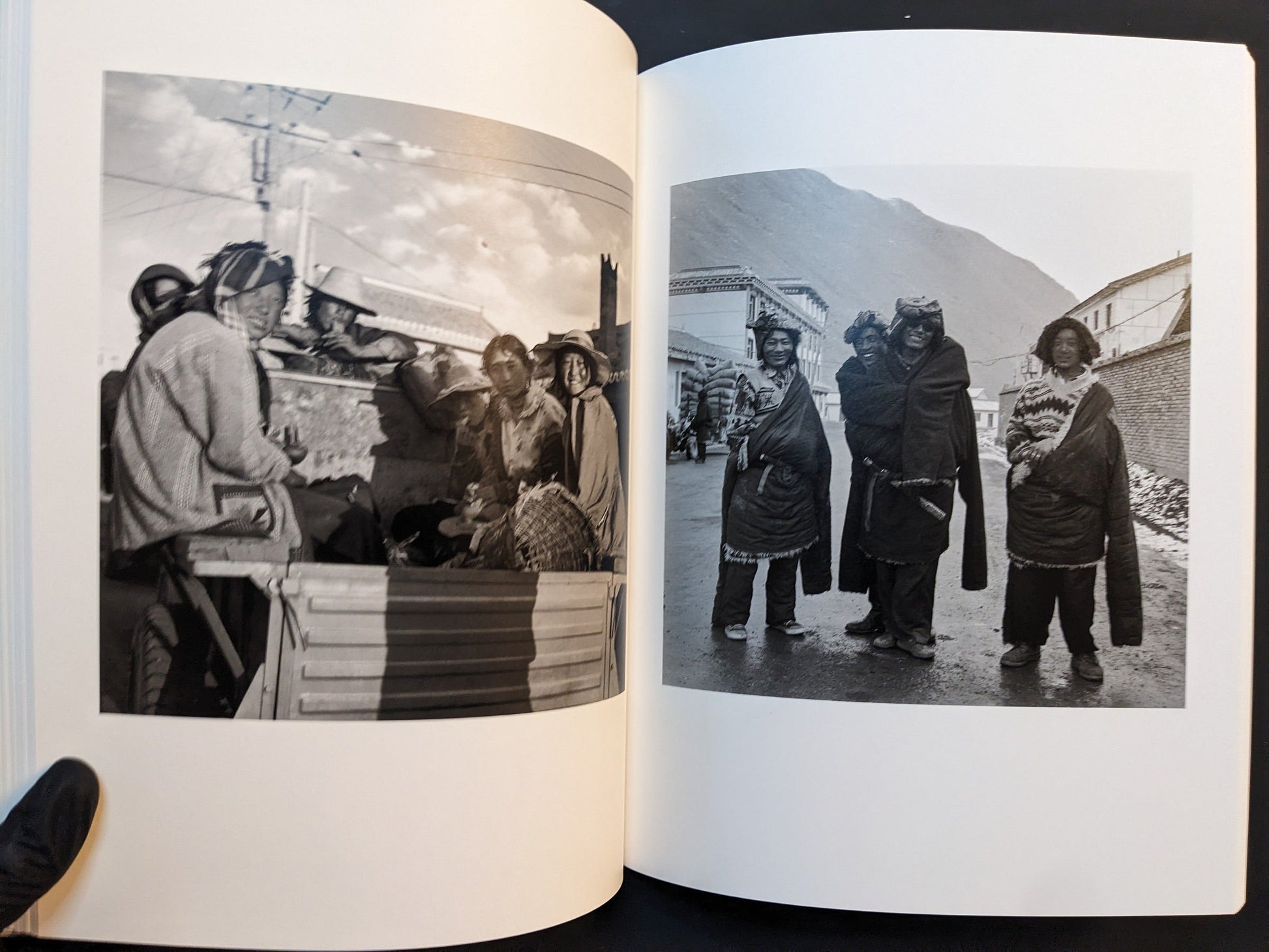 Spread from “TIBET” showing people riding in the back of a small truck in a village and a group of four figures standing together on a street.