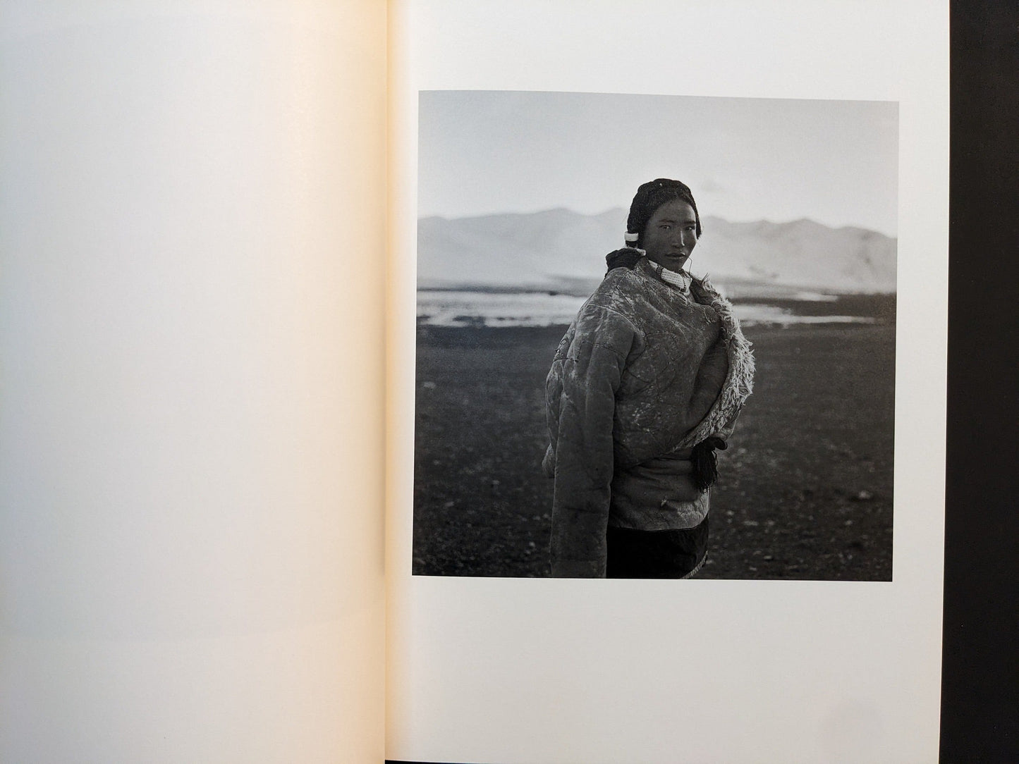 Inside page from Tibet with a woman in a heavy coat standing on a high plateau with mountains behind.