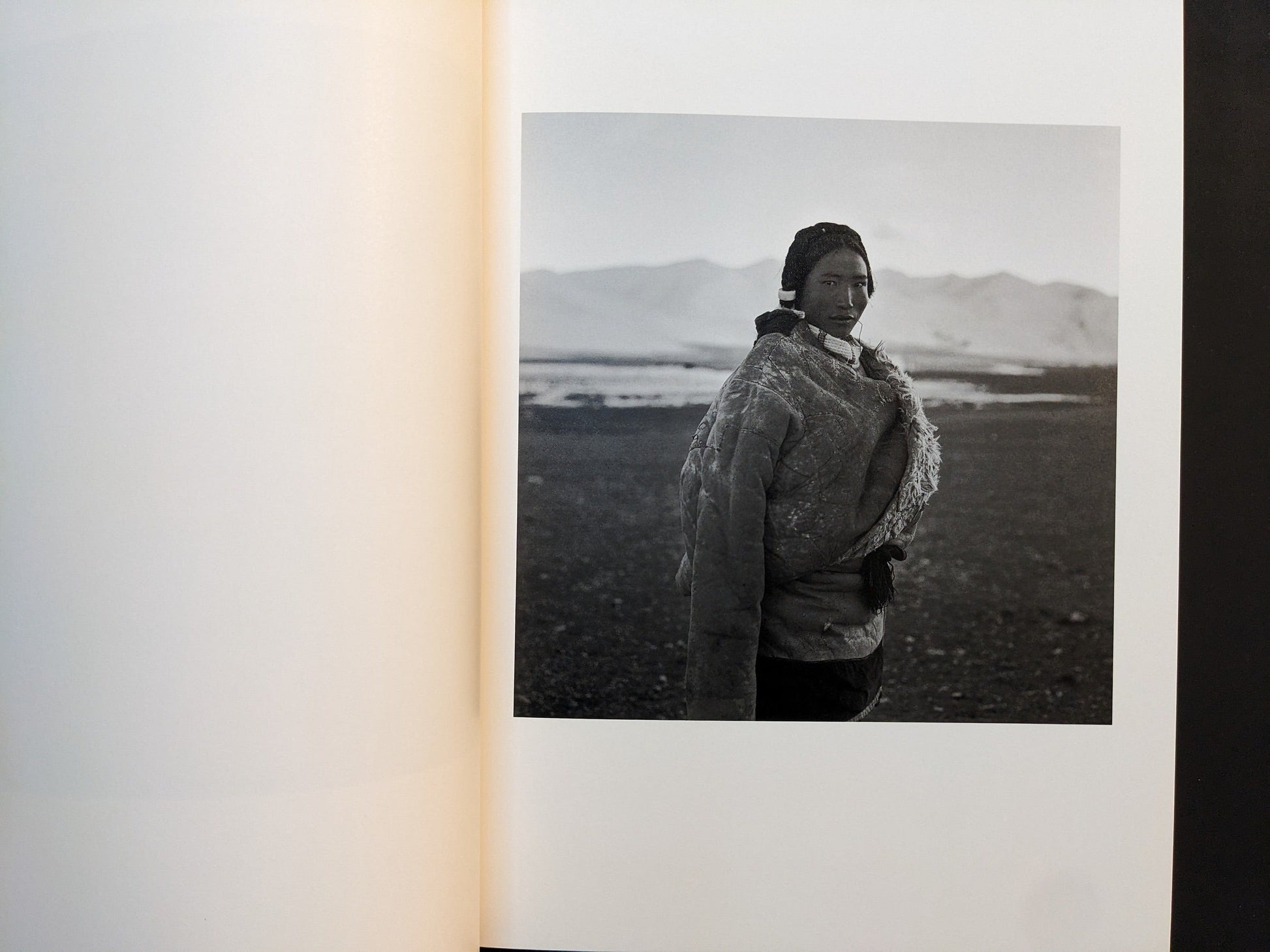 Inside page from Tibet with a woman in a heavy coat standing on a high plateau with mountains behind.