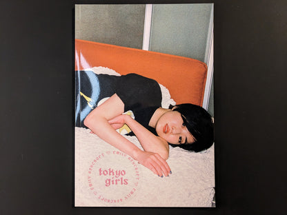 Front cover of Tokyo Girls by Emily Ashcroft, featuring a young woman lying on an orange bench, looking directly at the camera.