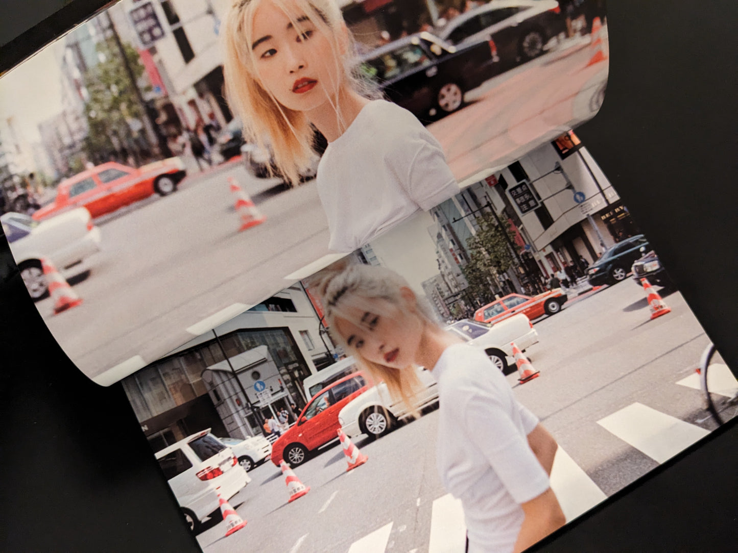 Blonde woman crossing a busy Tokyo street with taxis and traffic cones, city scene in the background.