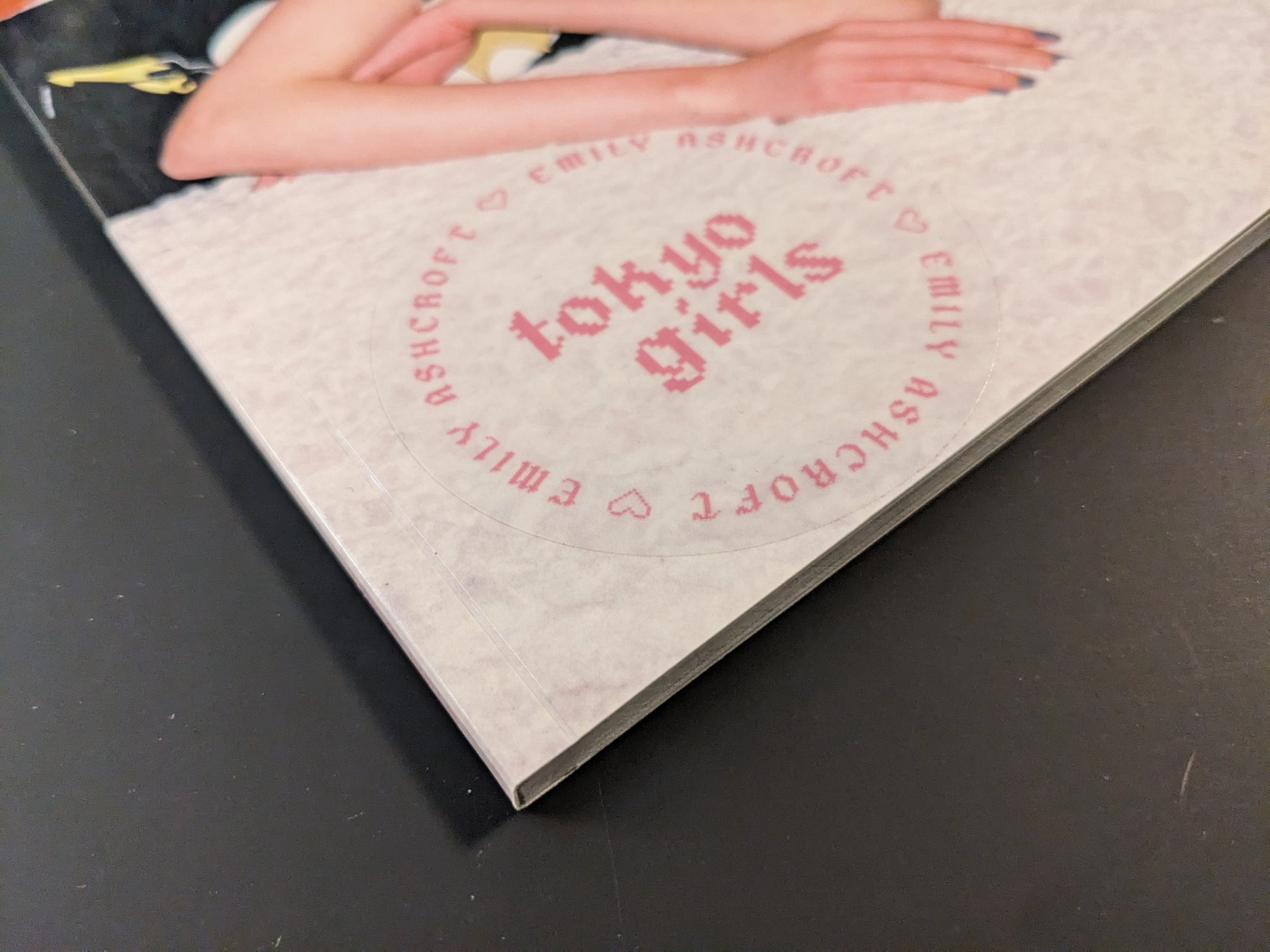 Close-up of the spine of the photobook "Tokyo Girls" by Emily Ashcroft, showing the title and pink circular logo