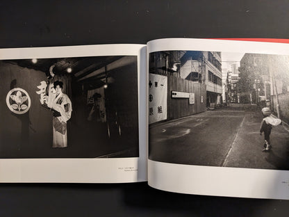 Spread from “Tokyo on the Brink of Sanity” with a stage performer in traditional costume holding a fan and a child wearing a helmet and bag walking alone down a narrow street.