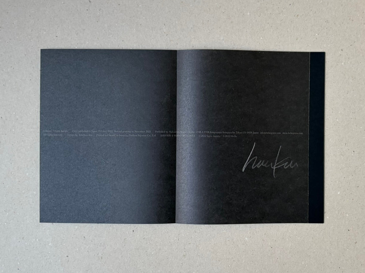 Open accordion-bound photobook spread from torikumo by Haruka Fujita, showing dark pages with small printed colophon text and a signature on the right page.