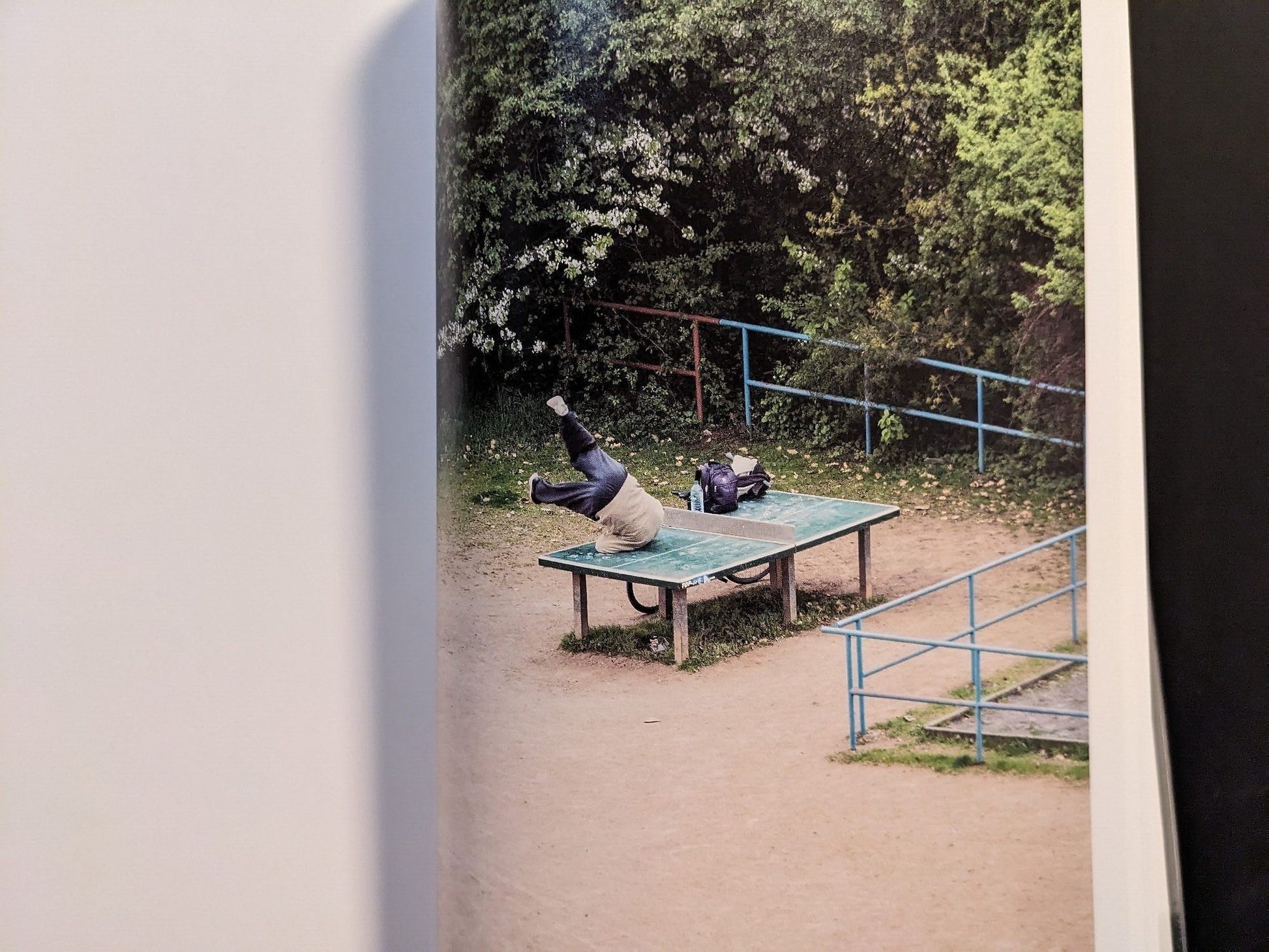 Photograph of a person reclining on the ping-pong table in a quiet outdoor scene.
