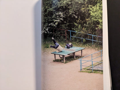 Photograph of a person reclining on the ping-pong table in a quiet outdoor scene.