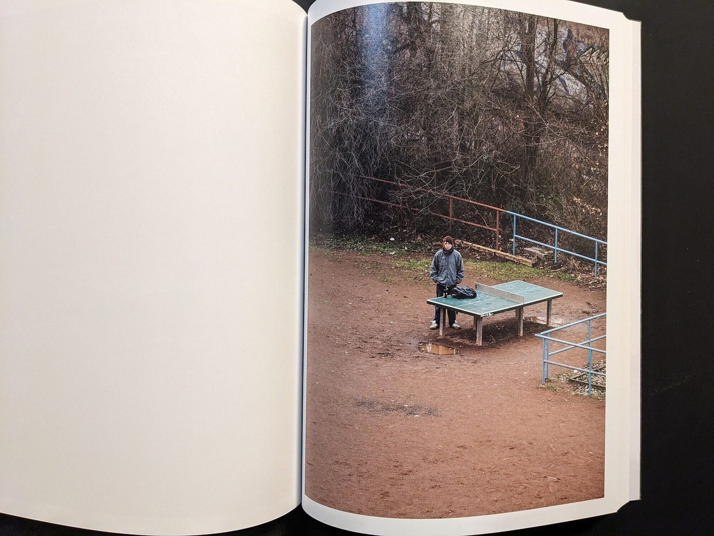 Photograph of a single person standing near the ping-pong table in an empty playground.