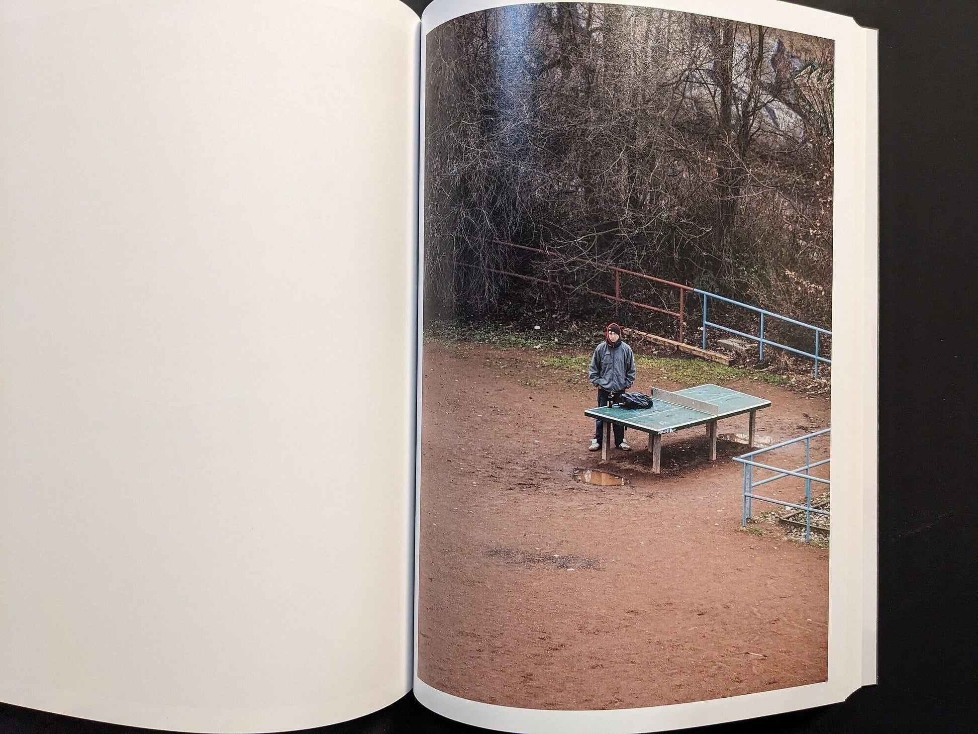Photograph of a single person standing near the ping-pong table in an empty playground.
