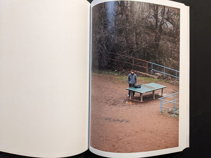 Photograph of a single person standing near the ping-pong table in an empty playground.