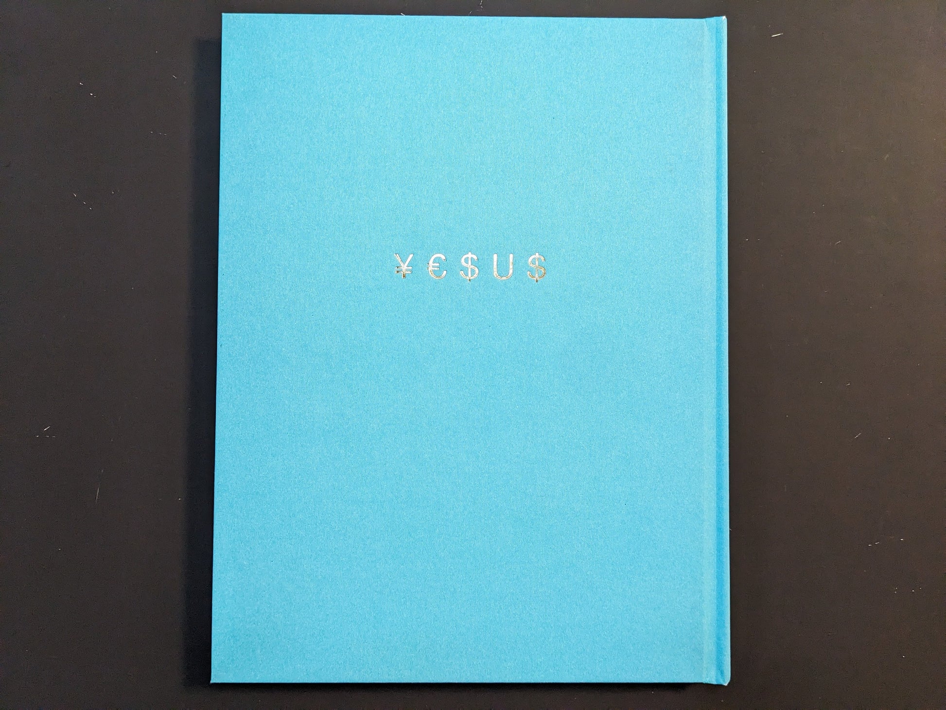 Back cover of ¥€$U$ (JESUS) by Pawel Jaszczuk, shown as a plain turquoise cloth hardcover with the title stamped in gold.