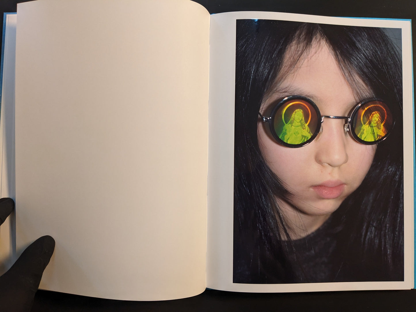 Open spread from ¥€$U$ (JESUS) showing a child wearing round glasses with reflected haloed saint images.