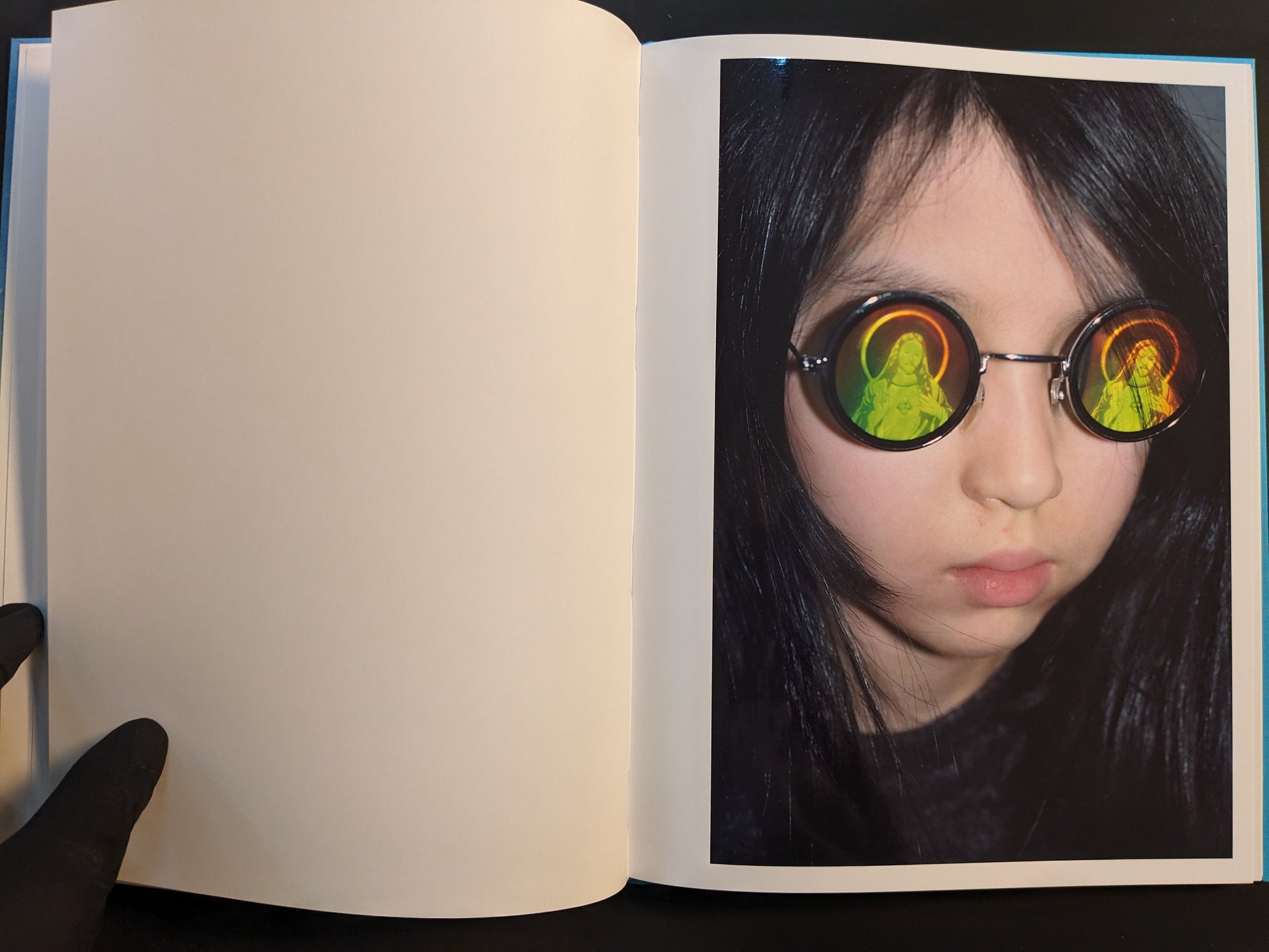 Open spread from ¥€$U$ (JESUS) showing a child wearing round glasses with reflected haloed saint images.