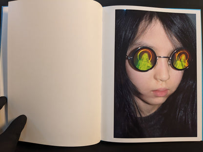 Open spread from ¥€$U$ (JESUS) showing a child wearing round glasses with reflected haloed saint images.